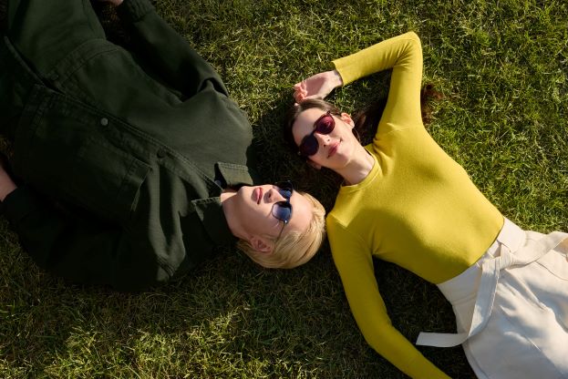 Due persone distese sull’erba indossano occhiali da sole, una con lenti blu e l’altra con lenti rosso scuro ZEISS