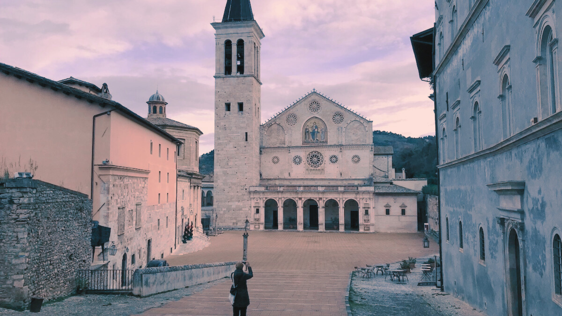 Piazza del Duomo a Spoleto con la Cattedrale di Santa Maria Assunta, il campanile romanico e una persona che fotografa la facciata.