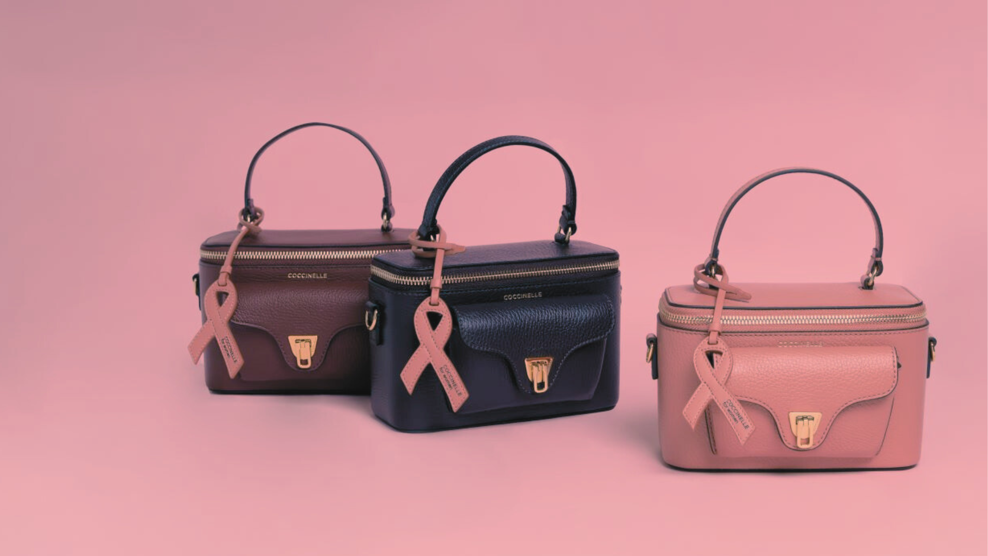Tremini bag Coccinelle Beat Generation con charm a nastro rosa, nei colori Ribes, Prune e Pink Clay, esposte su sfondo rosa.