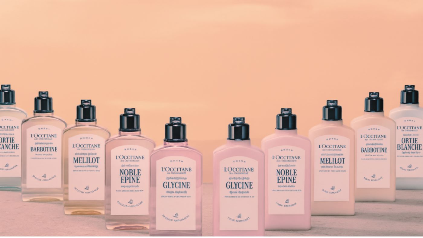Collezione Flora Orchestra di L’Occitane con flaconi e lozioni disposti su fondo color pesca, ispirati ai profumi floreali della Provenza.