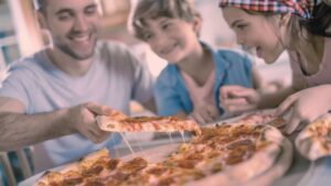 Famiglia sorridente che condivide una pizza appena sfornata con mozzarella filante attorno al tavolo di casa