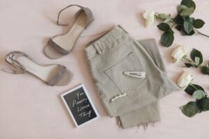 Flat lay con jeans beige, sandali chiari, mollette con perle e rose bianche su sfondo neutro