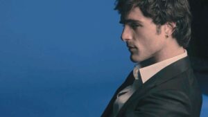 Ritratto laterale di Jacob Elordi per Chanel, in abito elegante su sfondo blu con luce soffusa e atmosfera sofisticata