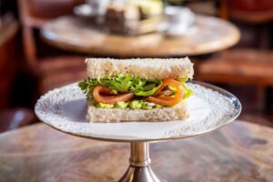 Tramezzino d’autore con salmone, insalata e crema verde servito su alzata all’interno del Caffè Mulassano