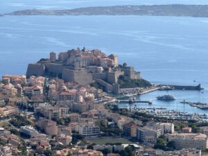 Veduta panoramica di Calvi, in Corsica, con la Cittadella fortificata, il porto turistico e il mare sullo sfondo.