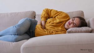Donna sdraiata sul divano con le mani sulla pancia per un dolore addominale.
