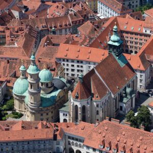 Veduta dall’alto dei tetti rossi del centro storico di Graz, con le cupole verdi e le torri delle chiese.