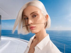 Modella bionda con pelle luminosa sullo sfondo del mare, protagonista della campagna solare Lancaster Monaco.
