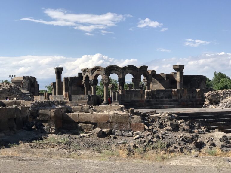 Rovine della Cattedrale di Zvartnots in Armenia, con antiche colonne e archi in pietra sotto un cielo azzurro.