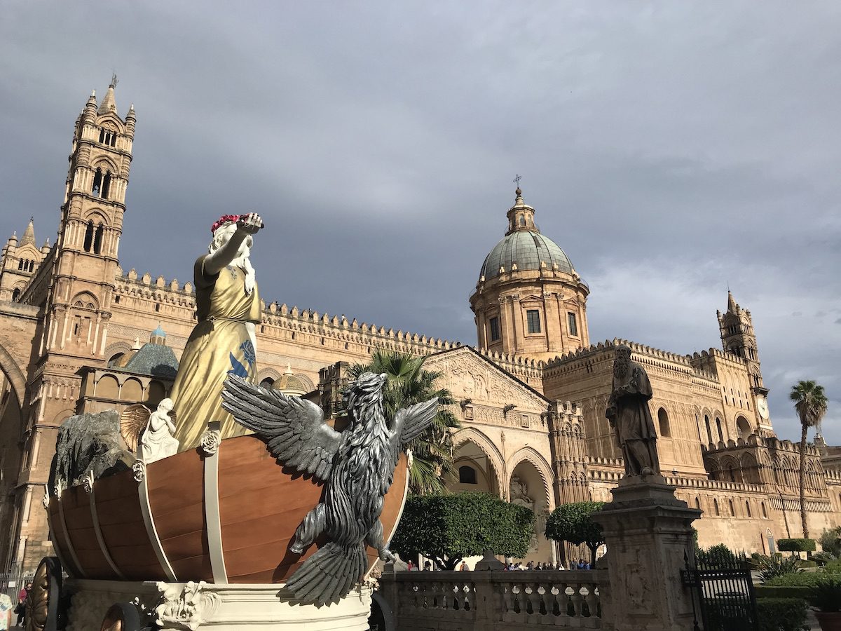 La Cattedrale di Palermo con le torri campanarie e la grande cupola, vista dalla piazza. In primo piano, un carro allegorico con una figura femminile e un'aquila dalle ali spiegate.
