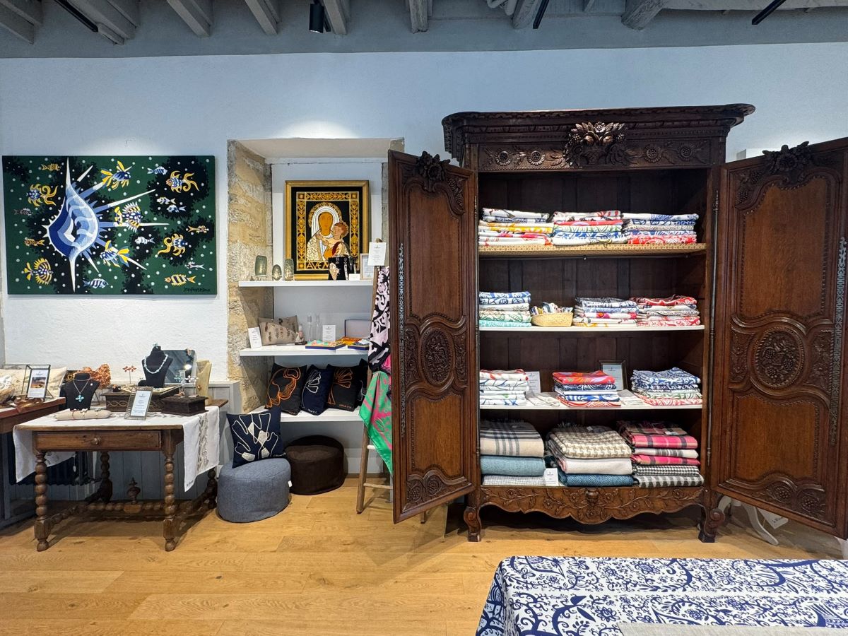 Interno dello spazio Le Minor, con un antico armadio in legno intagliato che custodisce tessuti colorati, accessori artigianali e oggetti decorativi.