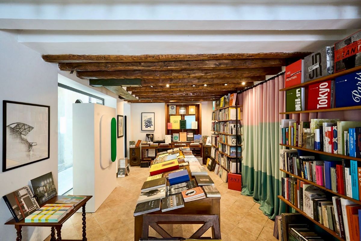 Interno della libreria Rupture Arts & Books a Venezia, con tavoli ricchi di libri d'arte, scaffali alle pareti e travi in legno a vista